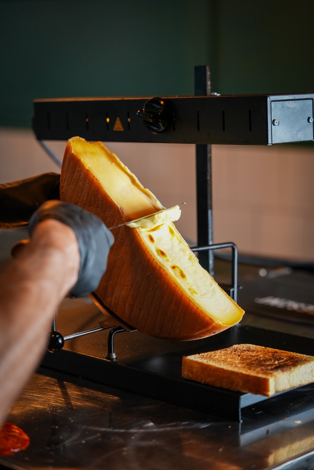Roztopiony ser raclette ścinany z kręgu na pieczywo